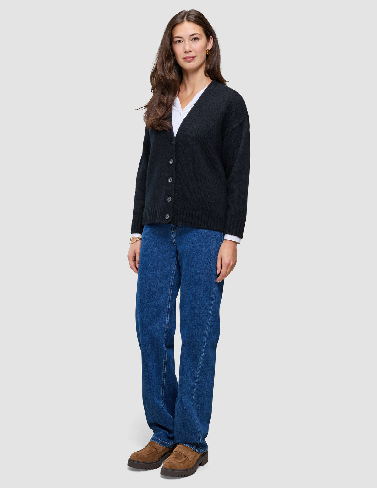 En kvinna som bär en svart, tjock och mjuk stickad kofta i ull från kollektionen Women över en vit skjorta och blå jeans.