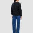 En person sedd bakifrån, klädd i en svart, tjock och mjuk stickad damkofta i ull över en vit skjorta och blå jeans.