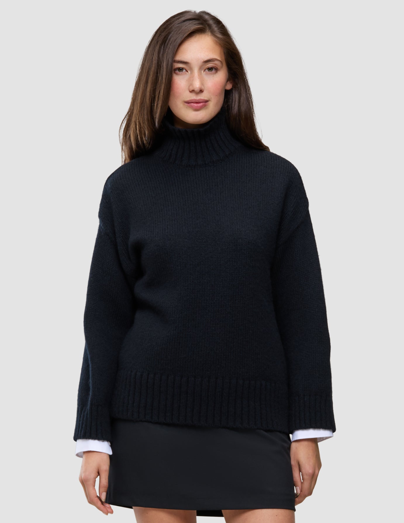 En kvinna klädd i en svart, tjock och mjuk stickad damtröja med hög hals i ull och skandinavisk design.