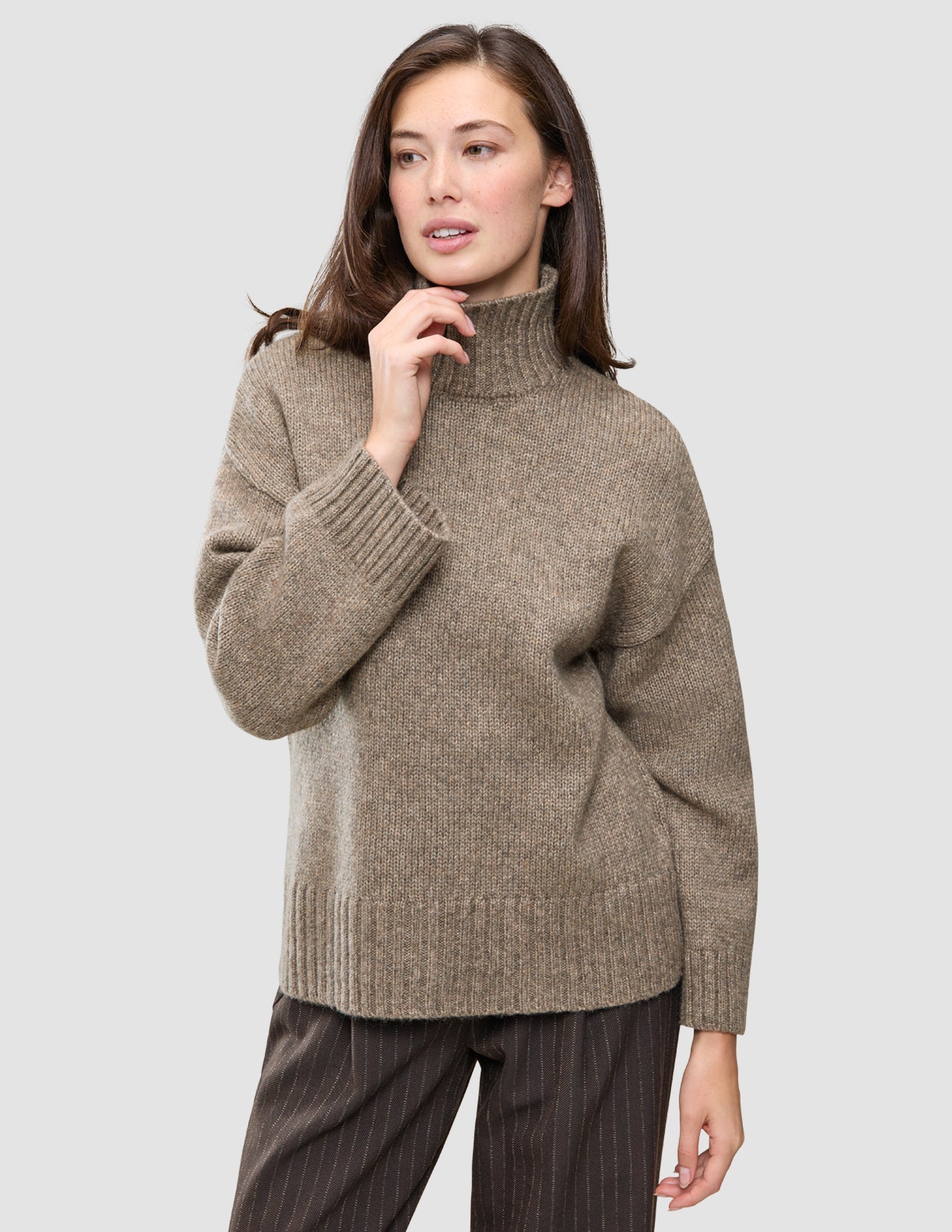 En kvinna klädd i en tjock, mjuk ullstickad turtleneck-tröja i färgen taupe melange från kollektionen Women.