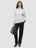 En kvinna klädd i en krämfärgad tröja med hög hals och svarta Women GO2 Pants Straight, som håller en svart handväska.