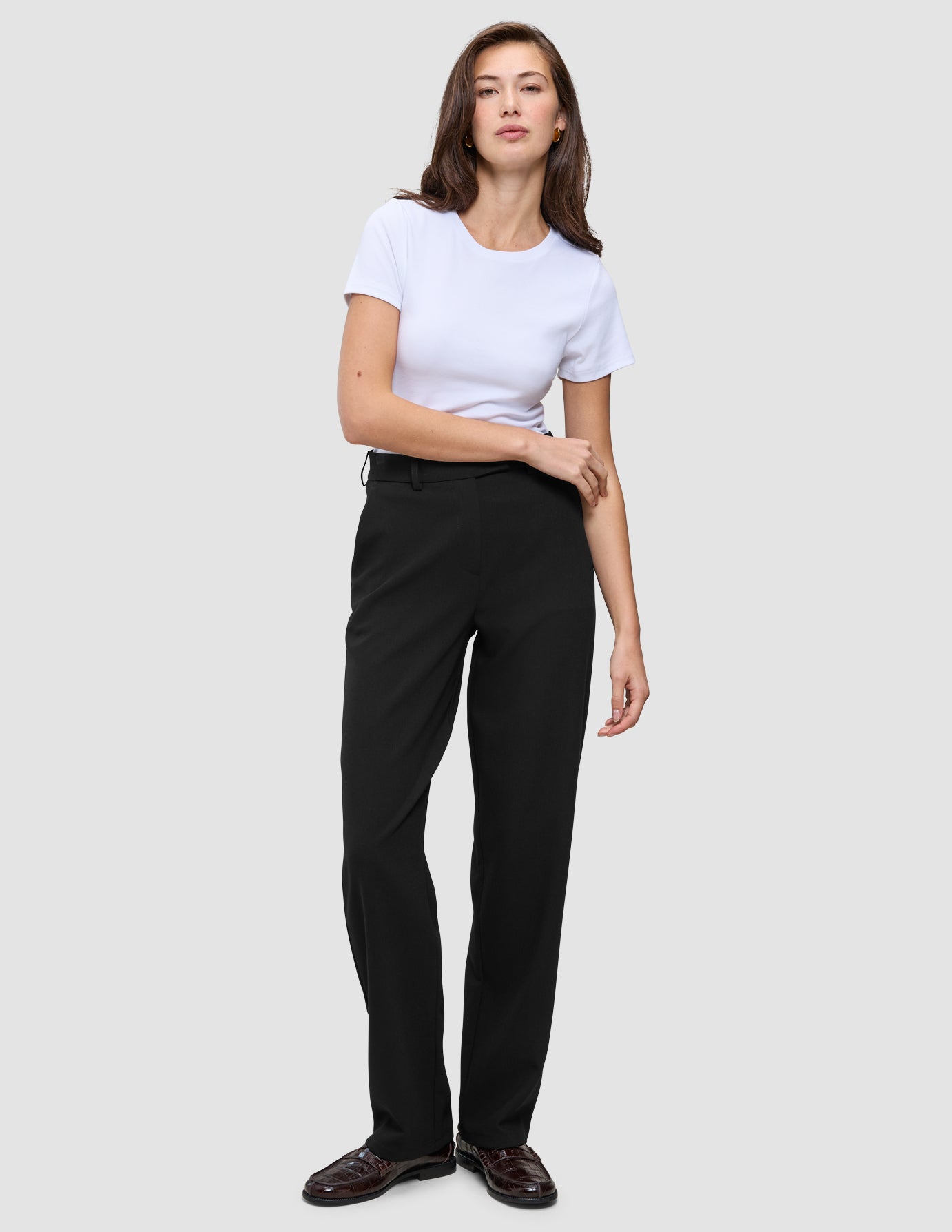 En kvinna klädd i en vit t-shirt, Women GO2 Pants Straight Black och mörka loafers i en ren skandinavisk design.