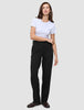 En kvinna klädd i en vit t-shirt, Women GO2 Pants Straight Black och mörka loafers i en ren skandinavisk design.