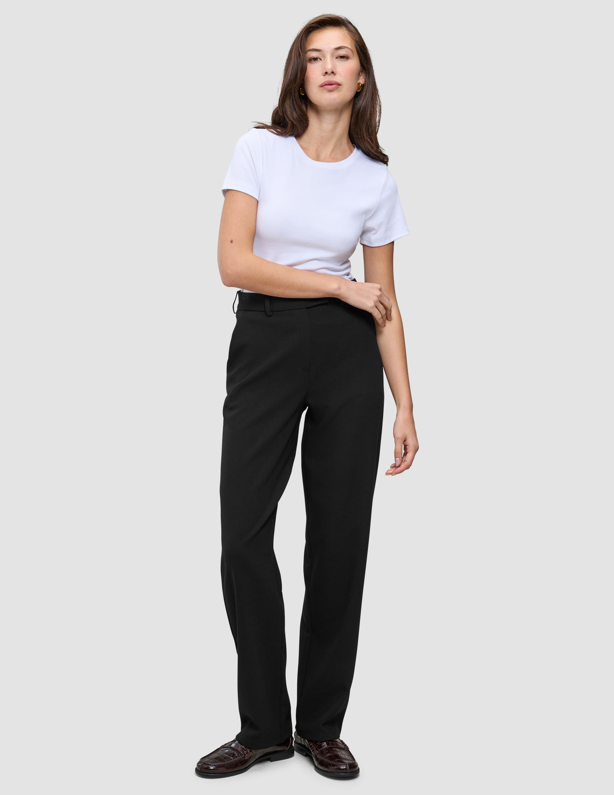 En kvinna klädd i en vit t-shirt, Women GO2 Pants Straight Black och mörka loafers i en ren skandinavisk design.