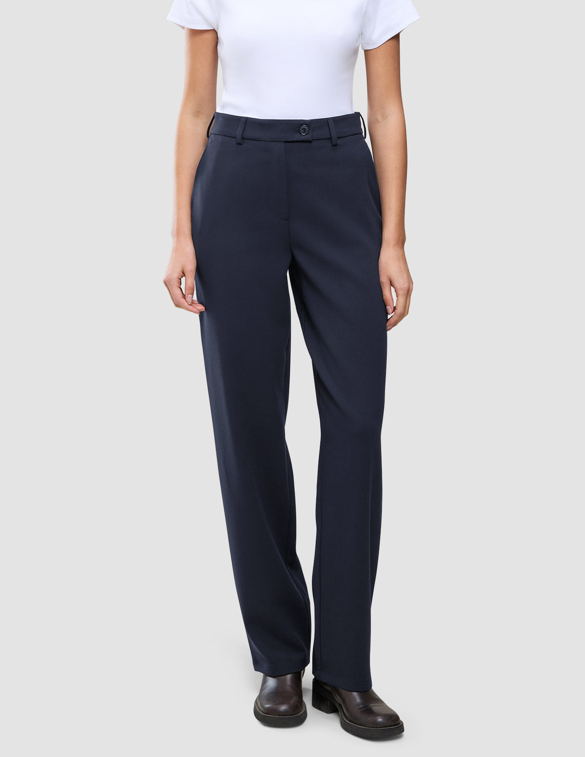 En person klädd i en vit t-shirt, Women GO2 Pants Straight Blue Nights och mörka skor, vilket återspeglar en skandinavisk estetik.