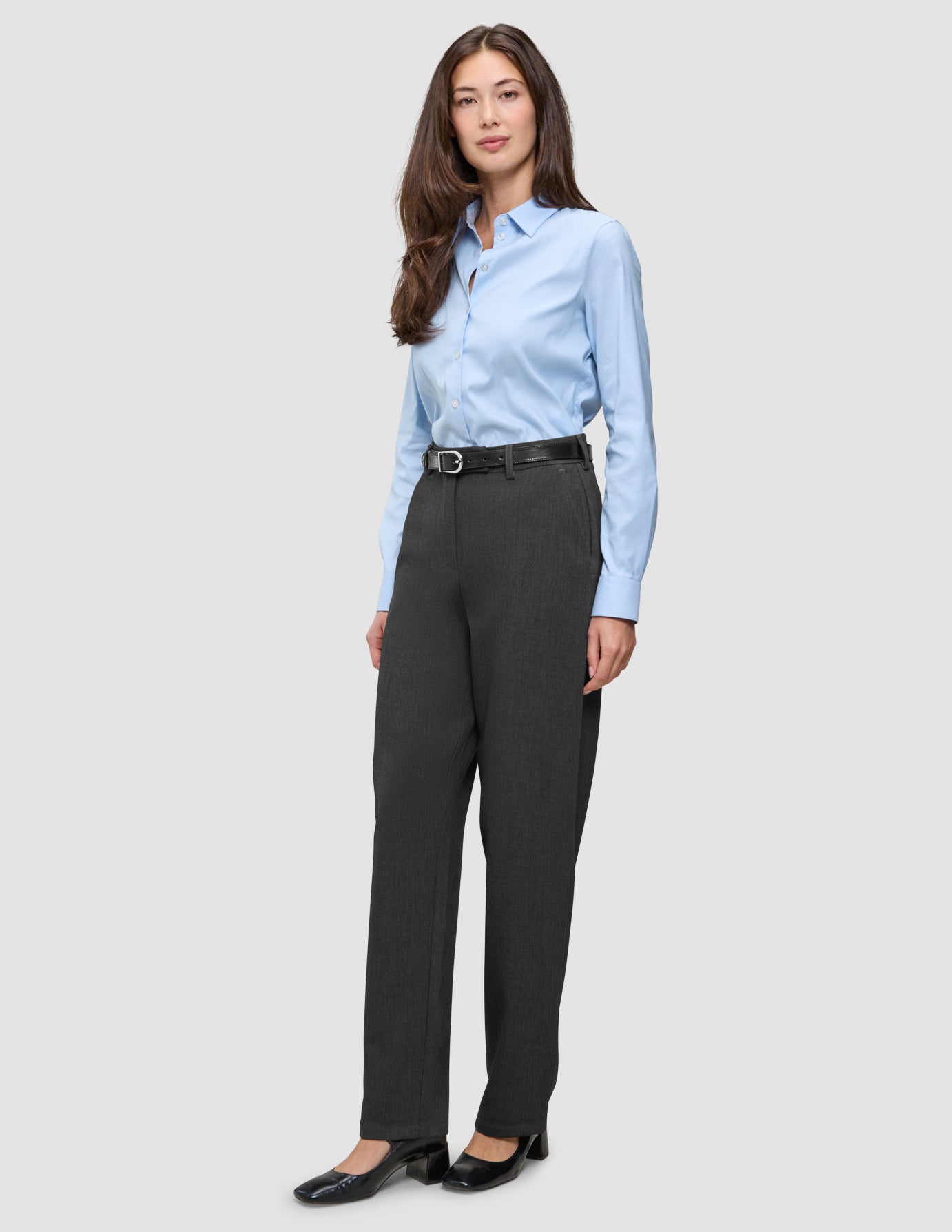 En kvinna i en ljusblå skjorta med knappar, svart bälte och byxor av modellen Women GO2 Pants Straight Dark Grey Melange i klassisk design.