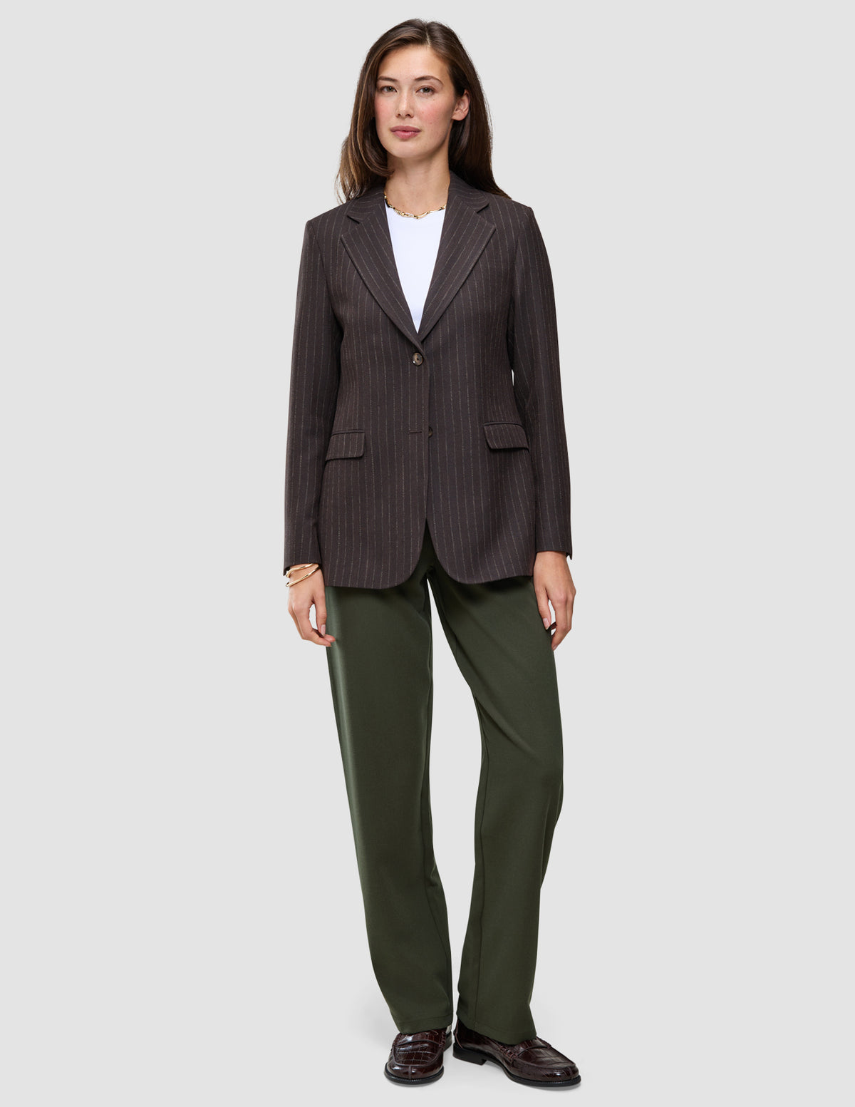 En mörkbrun blazer med smala ränder över en vit t-shirt, i kombination med Women GO2 Pants Straight Dusty Olive i klassisk design.