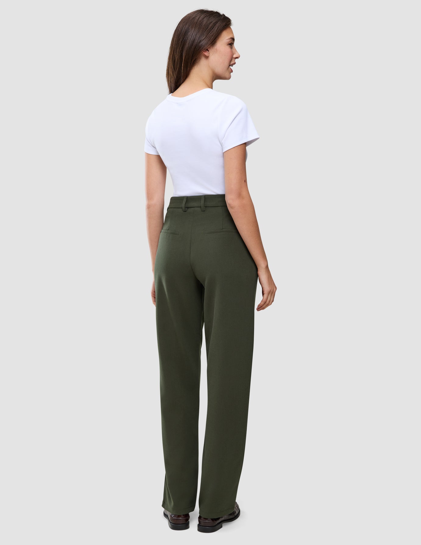 En kvinna sedd bakifrån, klädd i en vit t-shirt och raka byxor av modellen Women GO2 Pants Straight i färgen Dusty Olive.