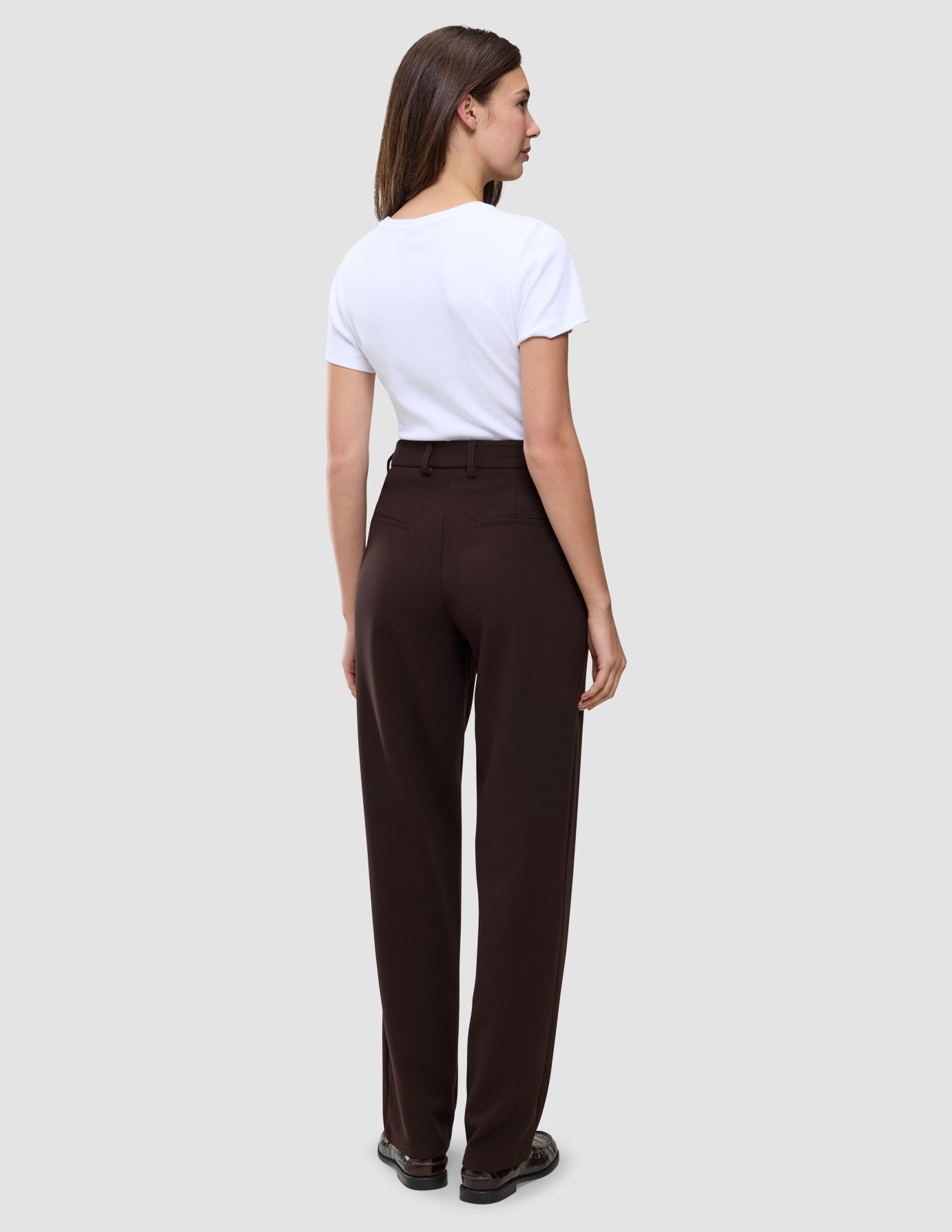 En kvinna sedd bakifrån, klädd i en vit t-shirt och Women GO2-byxor i färgen Mocha med raka ben.