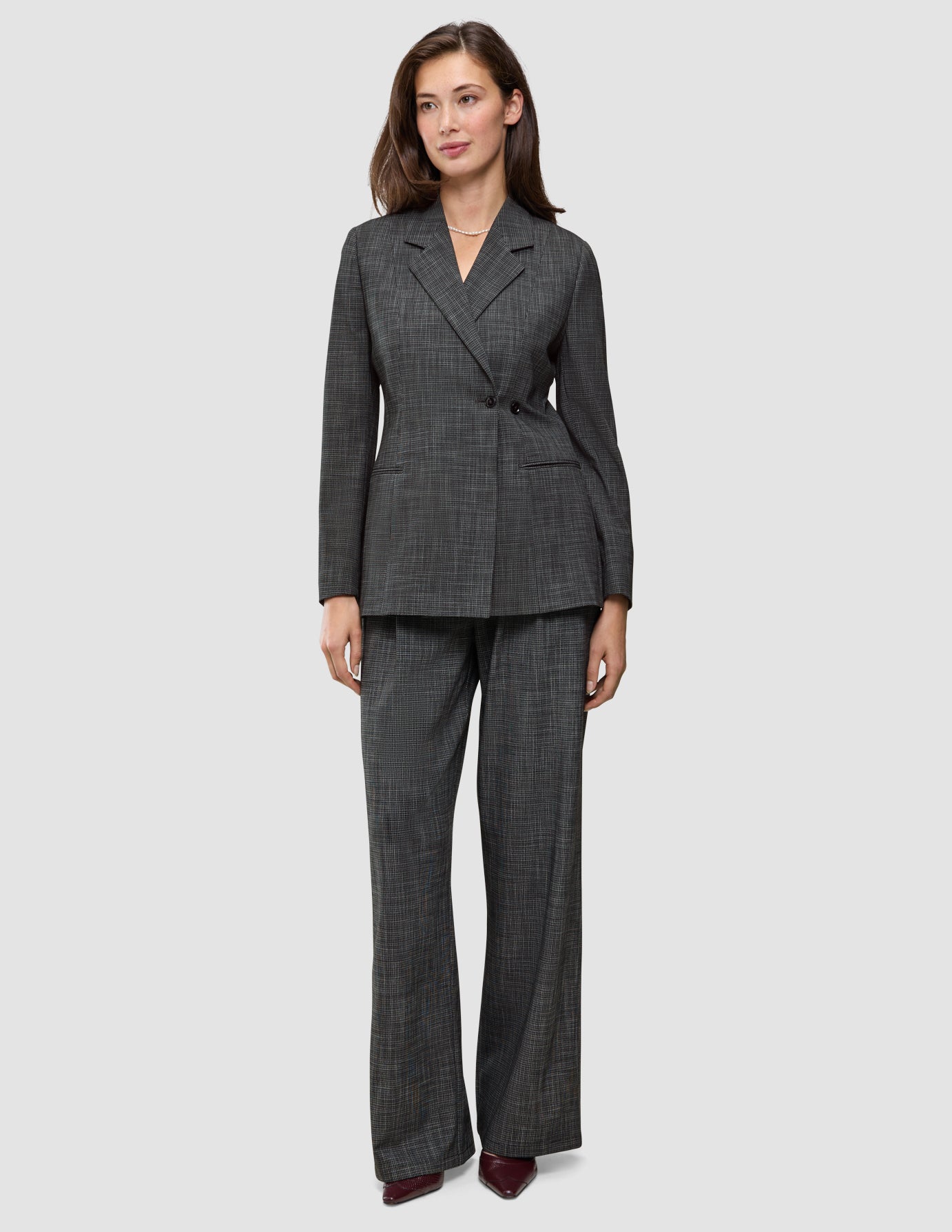En kvinna bär en Women Nara Blazer Fitted Black Check i mörkgrå rutmönster tillsammans med matchande byxor med vida ben och 360°-stretch.