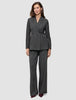 En kvinna bär en Women Nara Blazer Fitted Black Check i mörkgrå rutmönster tillsammans med matchande byxor med vida ben och 360°-stretch.
