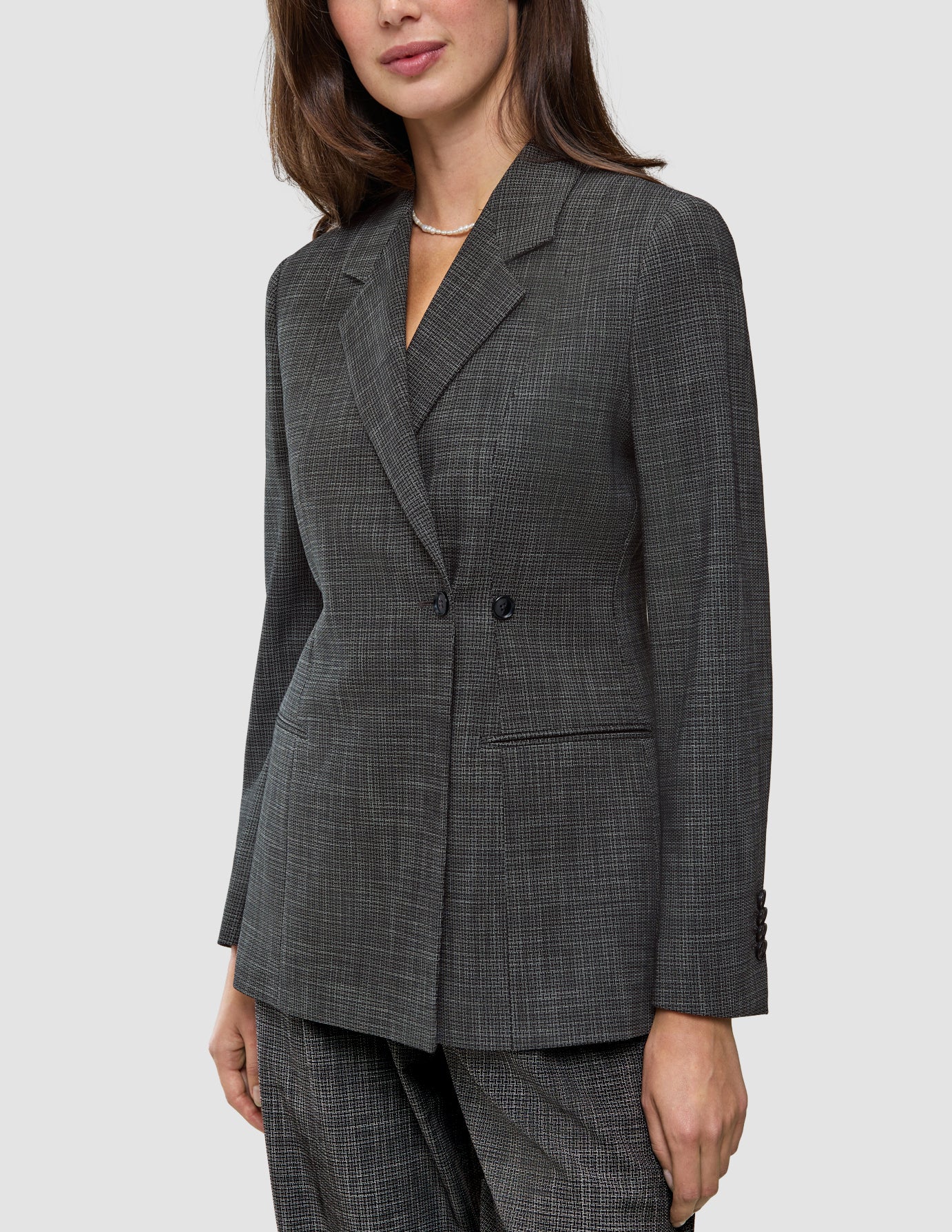 En kvinna bär en Women Nara Blazer Fitted Black Check, en skräddarsydd, svart- och vitrutig blazer med dubbelknäppning.