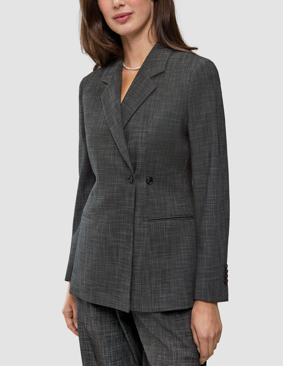 En kvinna bär en Women Nara Blazer Fitted Black Check, en skräddarsydd, svart- och vitrutig blazer med dubbelknäppning.