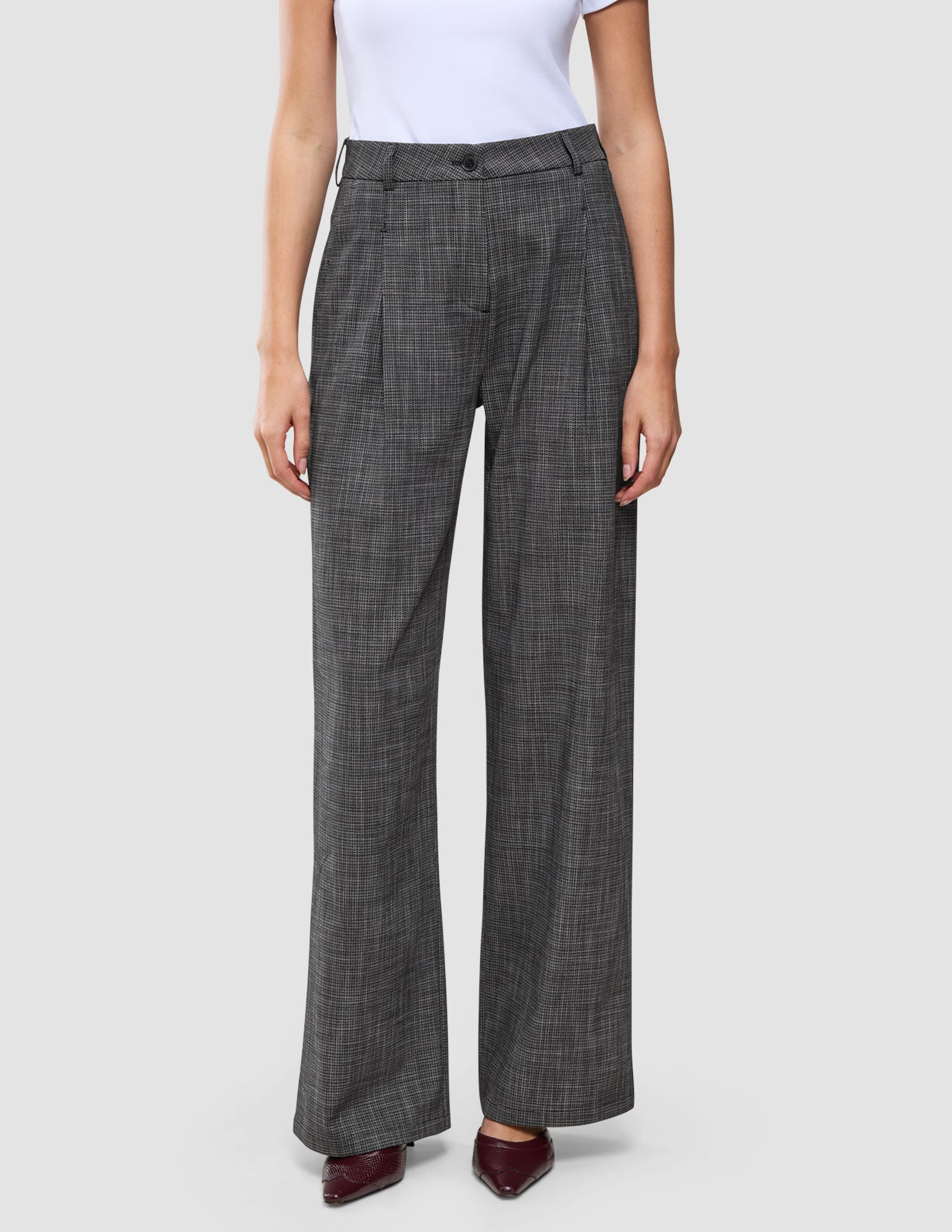 En person som bär ett par högmidjade Nara-byxor för damer, modell Wide Black Check, med ett kolgrått rutmönster.