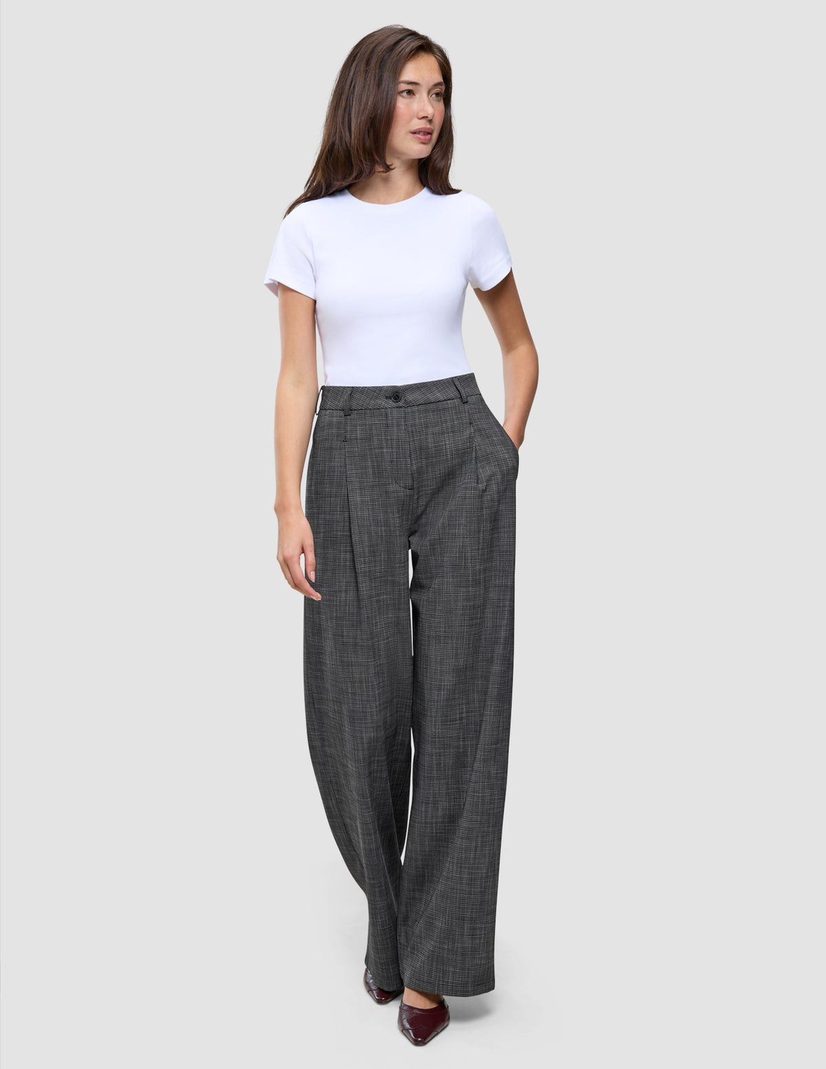 Kvinna klädd i en vit t-shirt och byxor av modellen Nara Pants Wide Black Check med ett diskret mönster.