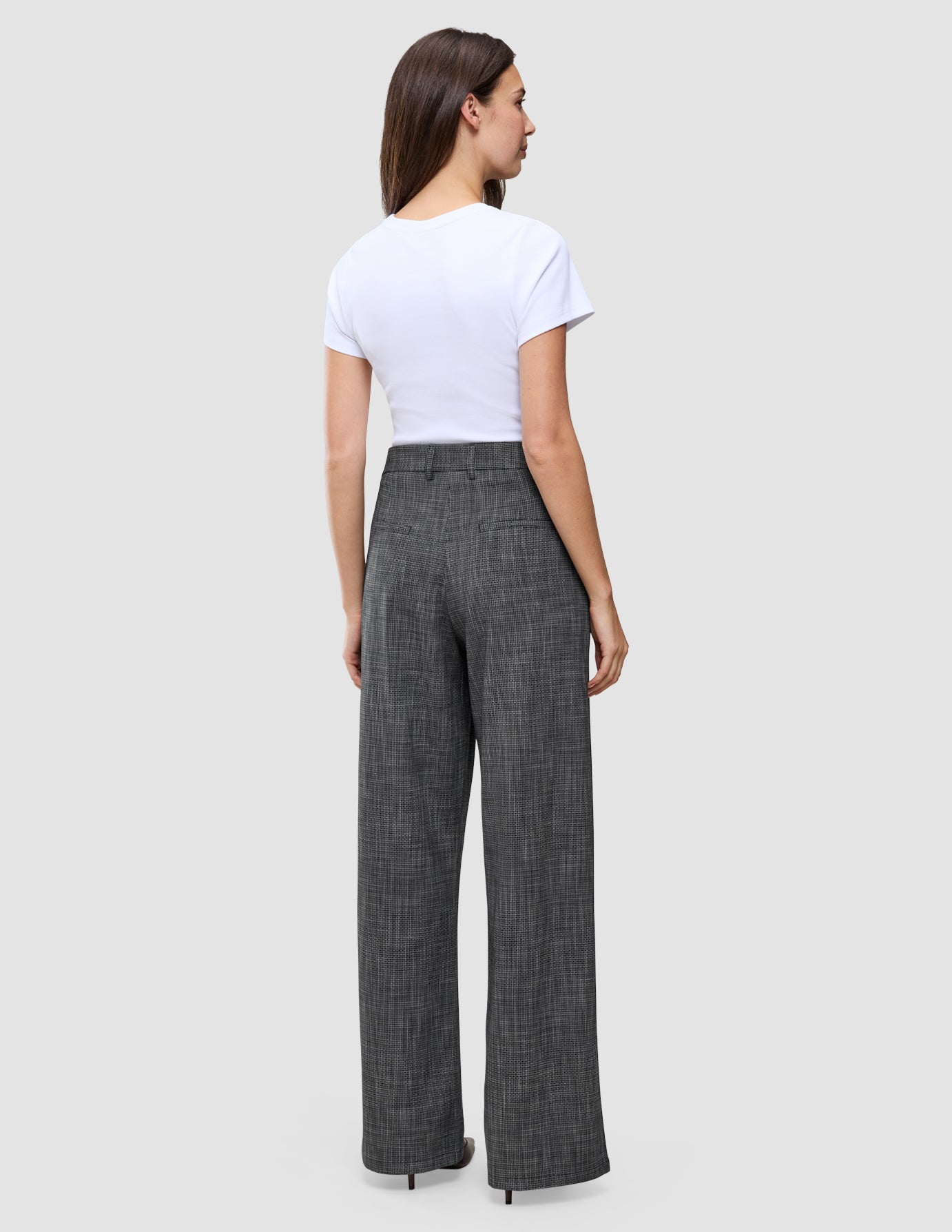 En kvinna sedd bakifrån, klädd i en vit t-shirt och byxor av modellen Women Nara Pants Wide Black Check med mörkgrå rutmönster.