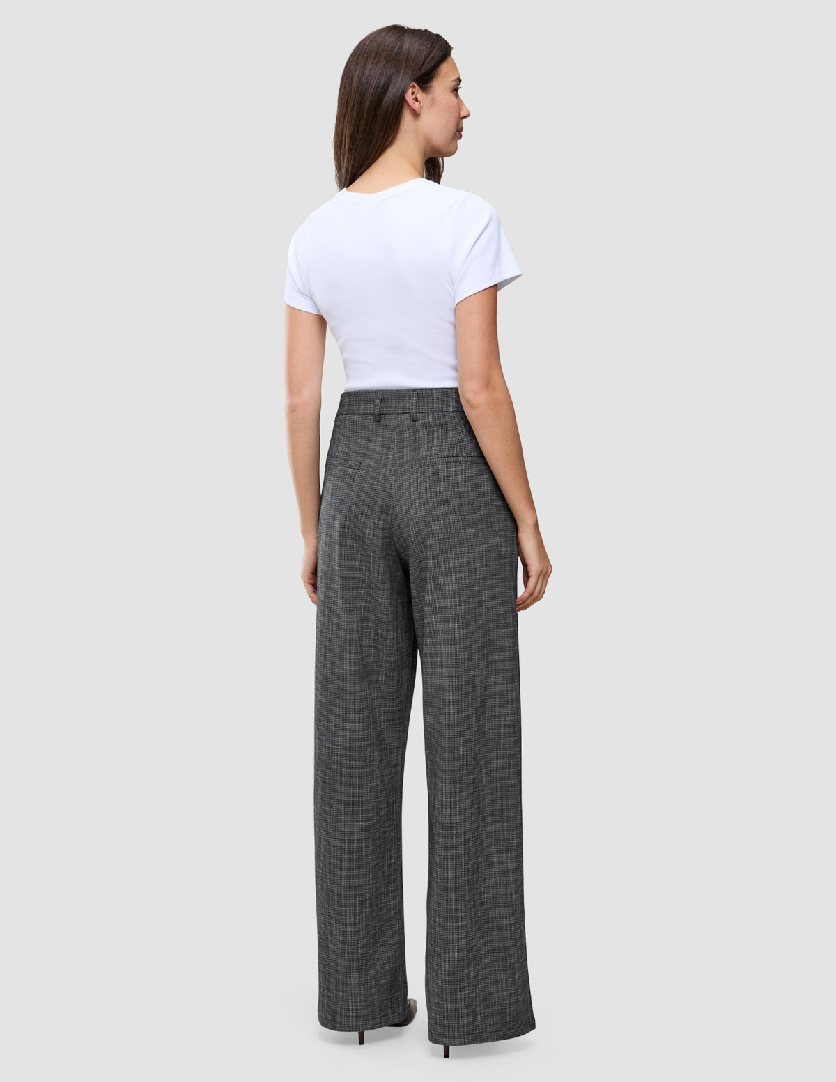 En kvinna sedd bakifrån, klädd i en vit t-shirt och byxor av modellen Women Nara Pants Wide Black Check med mörkgrå rutmönster.