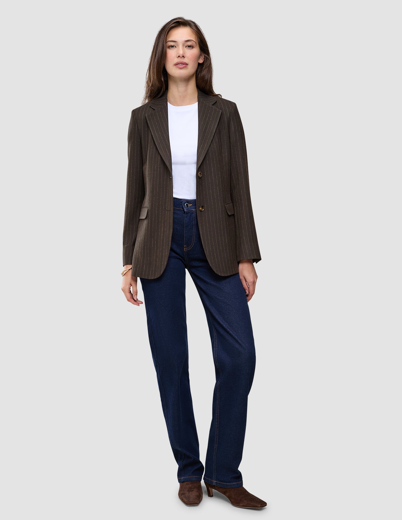 En kvinna bär en Women Serene Blazer Regular Walnut Herringbone, en vit t-shirt och mörkblå jeans.