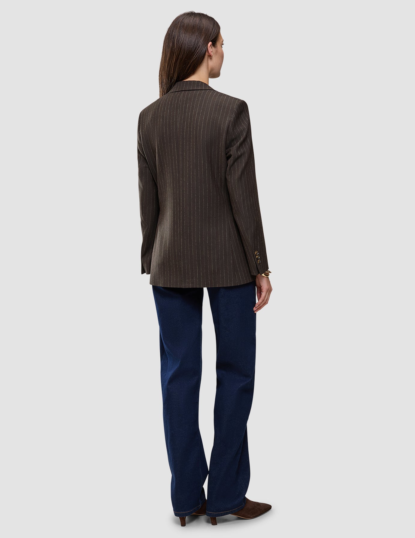 Bakifrånbild av en person klädd i en Women Serene Blazer Regular Walnut Herringbone, mörkblå jeans och bruna skor med ullfinish.