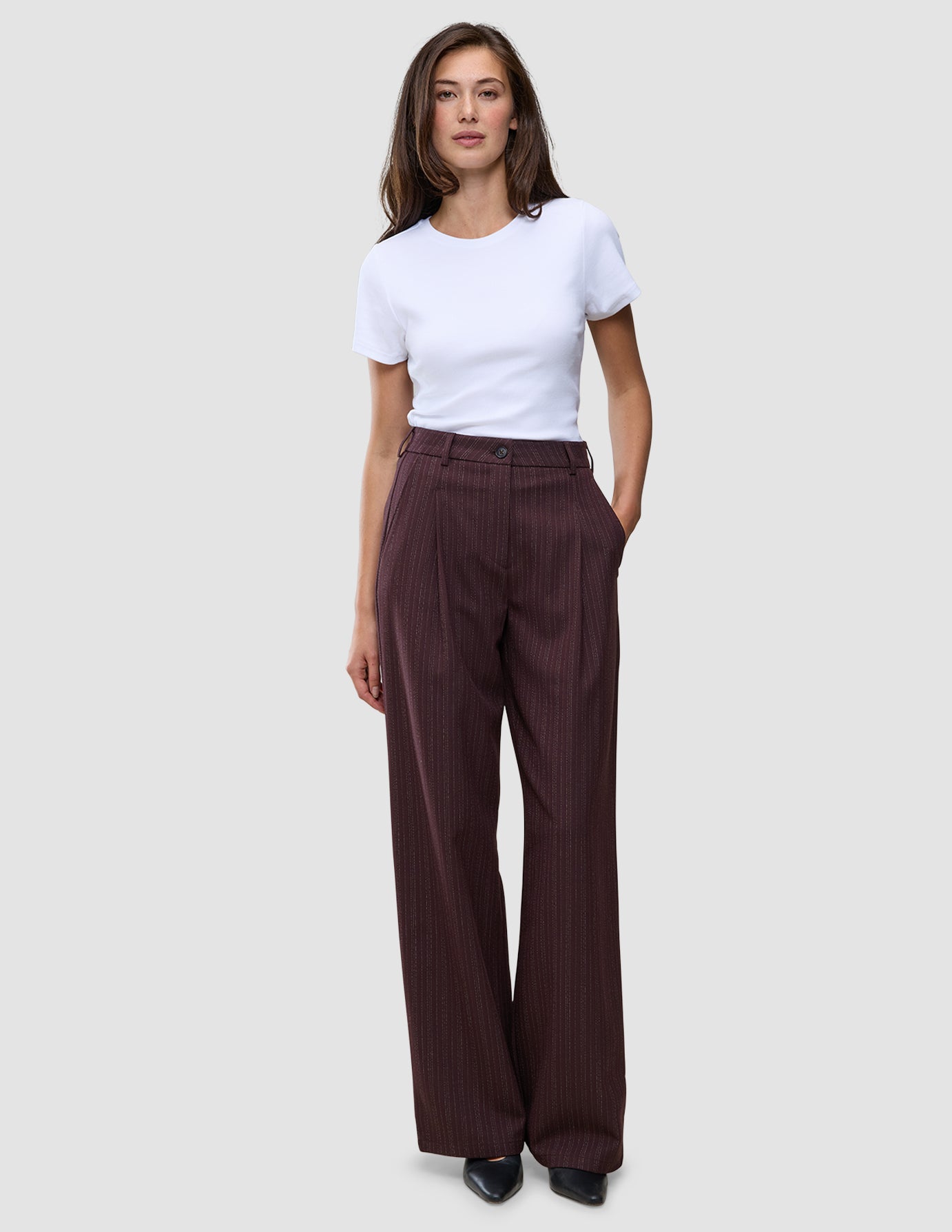 En kvinna bär en vit t-shirt och byxorna Women Serene Pants Wide Berry Pinstripe, som har vid ben och en minimalistisk design.