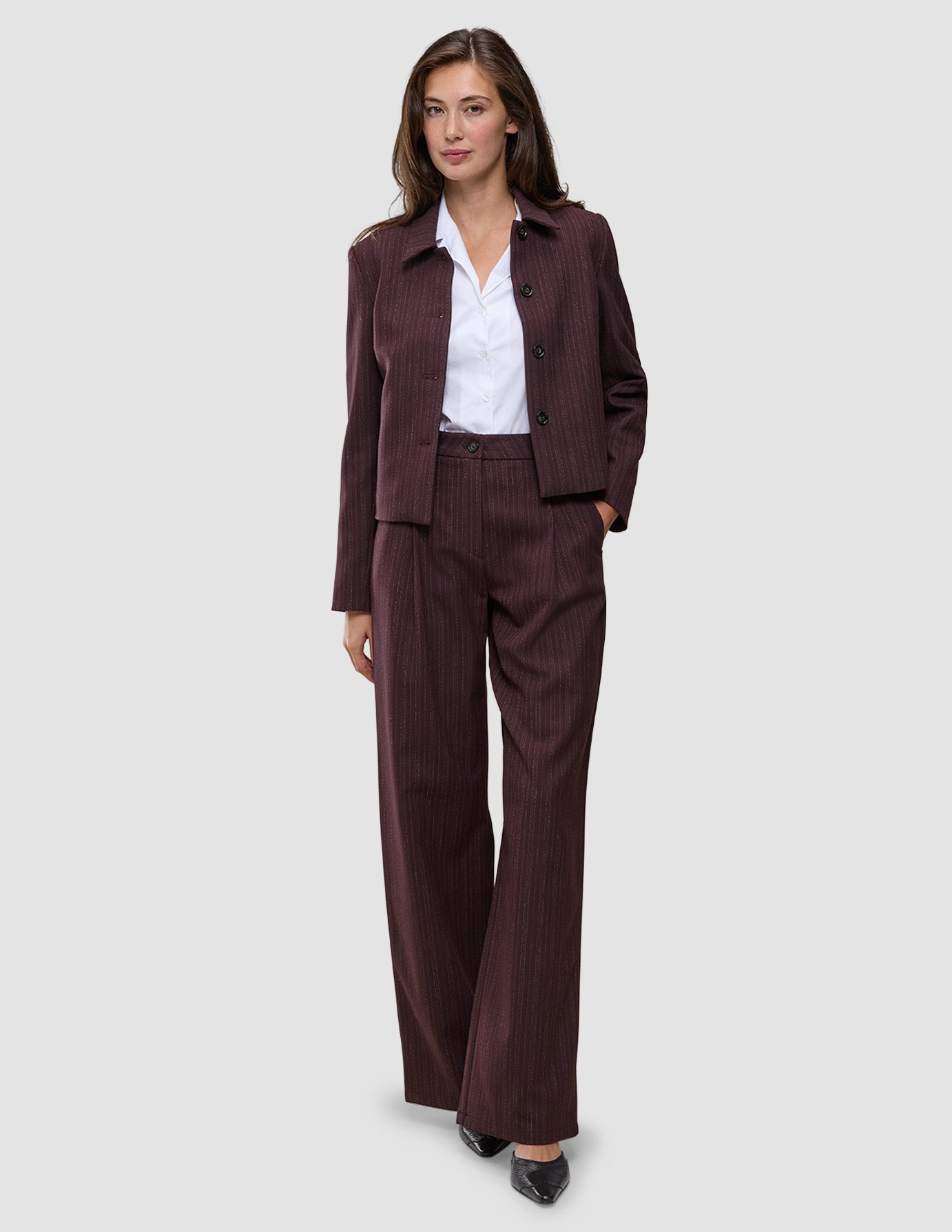 En kvinna bär en vinröd blazer med smala ränder och byxorna Women Serene Pants Wide Berry Pinstripe över en vit skjorta med krage.