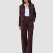 En kvinna bär en vinröd blazer med smala ränder och byxorna Women Serene Pants Wide Berry Pinstripe över en vit skjorta med krage.