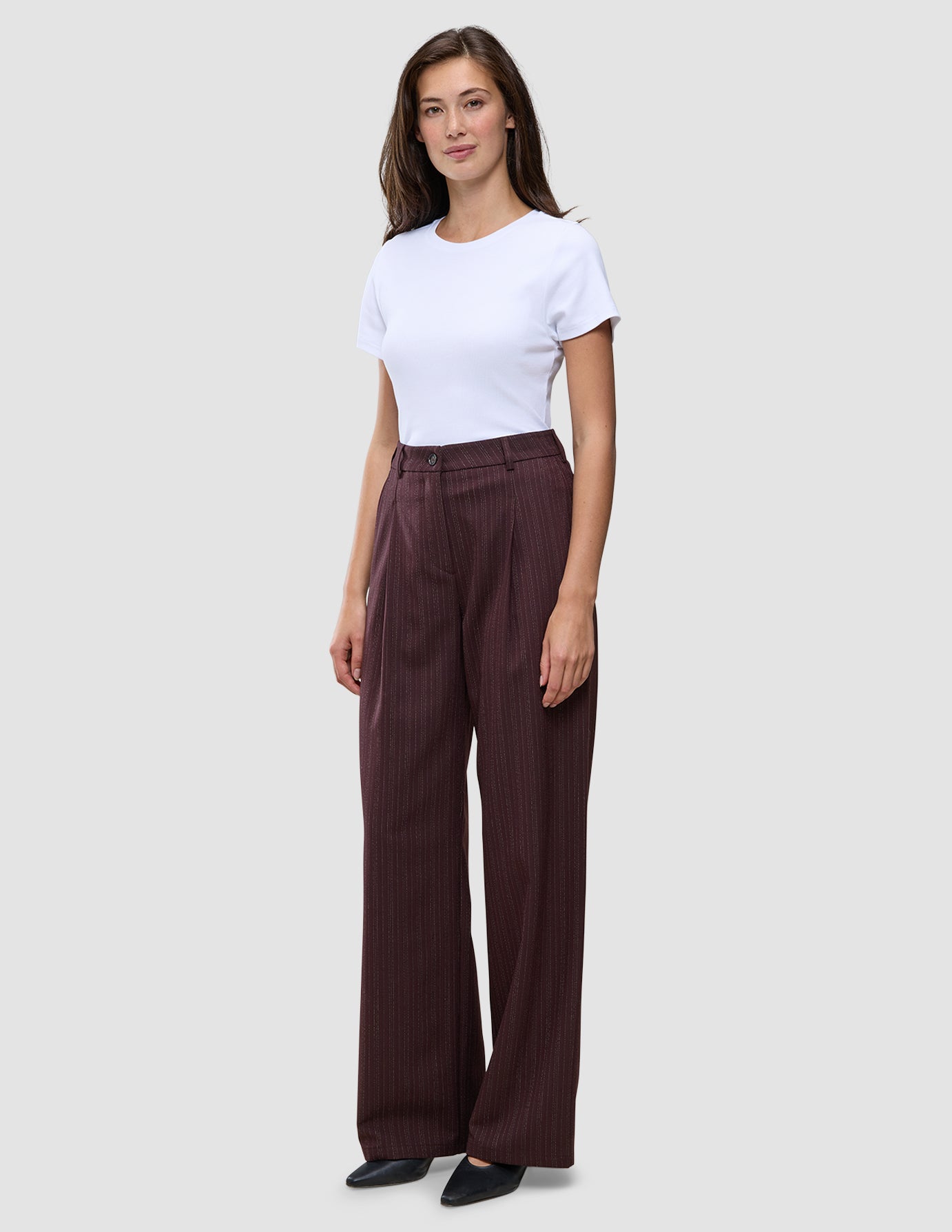 En person i en vit t-shirt och byxorna Women Serene Pants Wide Berry Pinstripe i mörkrött tyg med smala ränder.