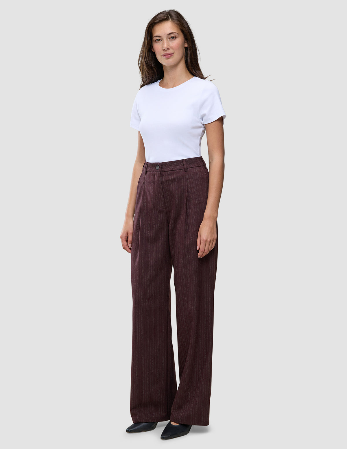 En person i en vit t-shirt och byxorna Women Serene Pants Wide Berry Pinstripe i mörkrött tyg med smala ränder.
