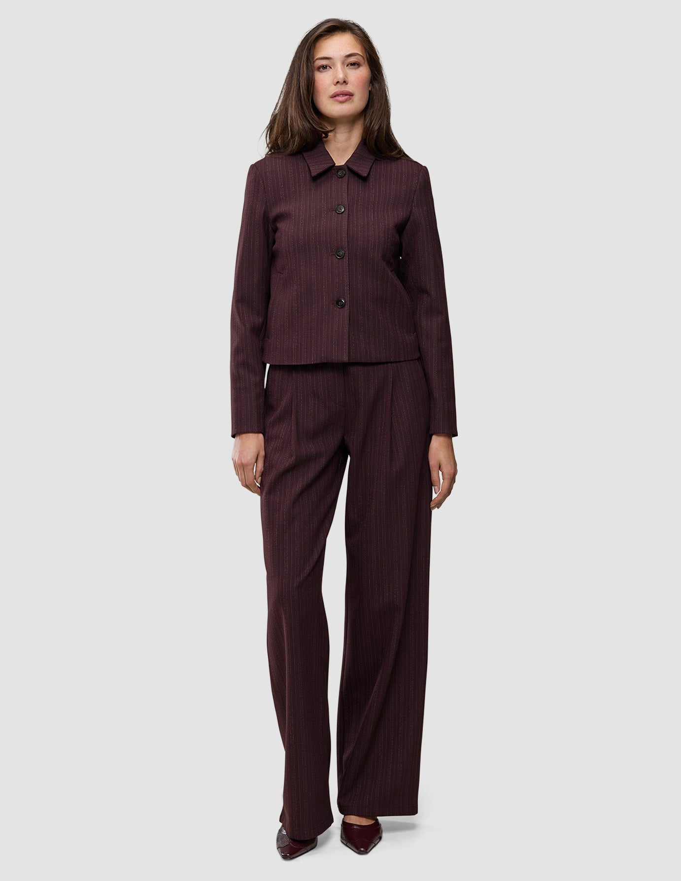 En kvinna bär en kort jacka av modellen Women Serene i färgen Berry Pinstripe tillsammans med matchande byxor med vida ben i skandinavisk design.