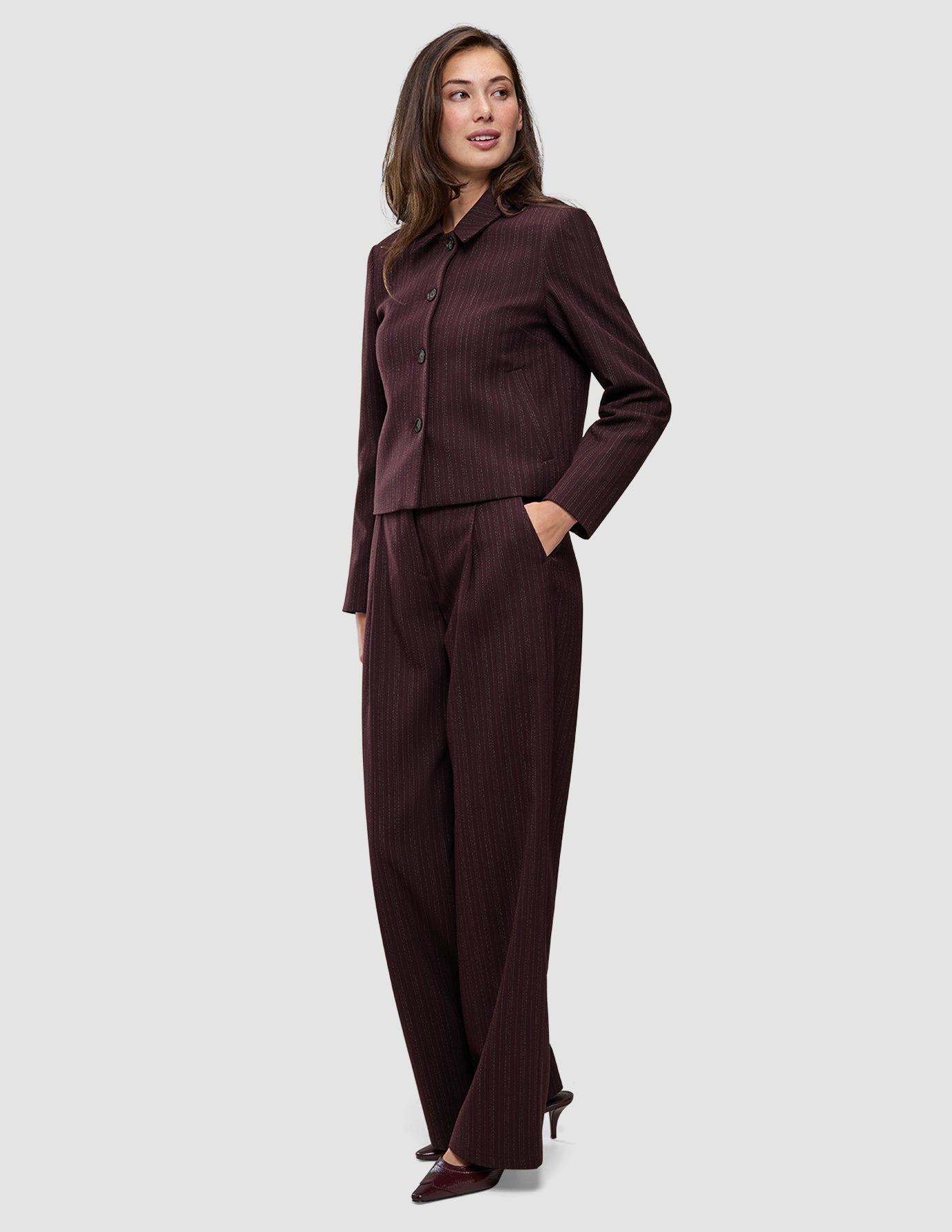 En kvinna bär en kort jacka av modellen Women Serene i färgen Berry Pinstripe tillsammans med matchande byxor med vida ben i skandinavisk design.