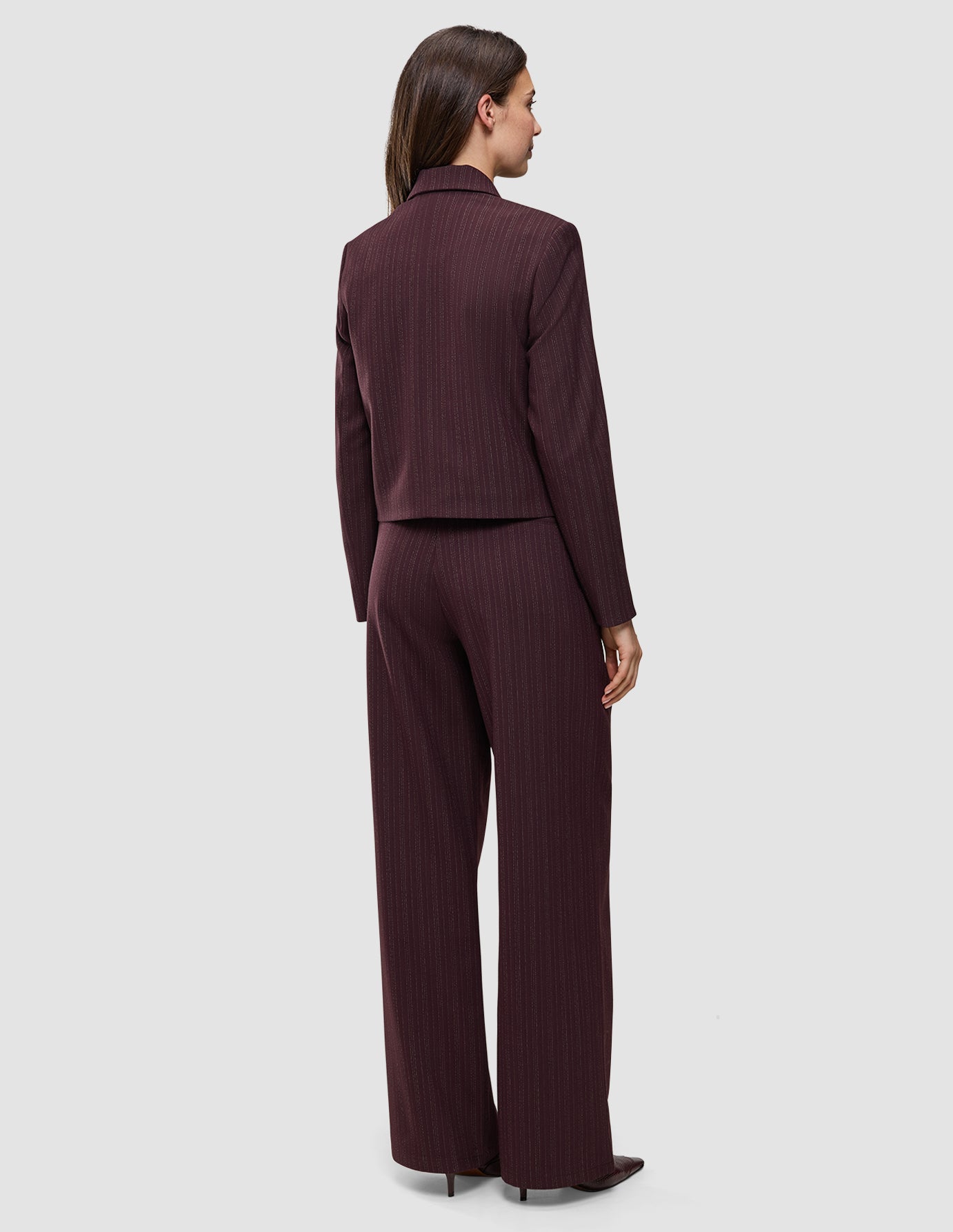 En kvinna sedd bakifrån, klädd i en kort jacka av modellen Women Serene Short Jacket Berry Pinstripe och matchande byxor med vida ben.