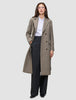 En person klädd i en lång, dubbelknäppt taupefärgad ullkappa i modell Women Wool Coat Greige över en vit skjorta och svarta byxor.